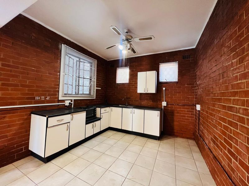 A functional kitchen featuring exposed brick walls, tiled flooring, and white cabinetry with dark countertops, offering a blank canvas for modern updates.