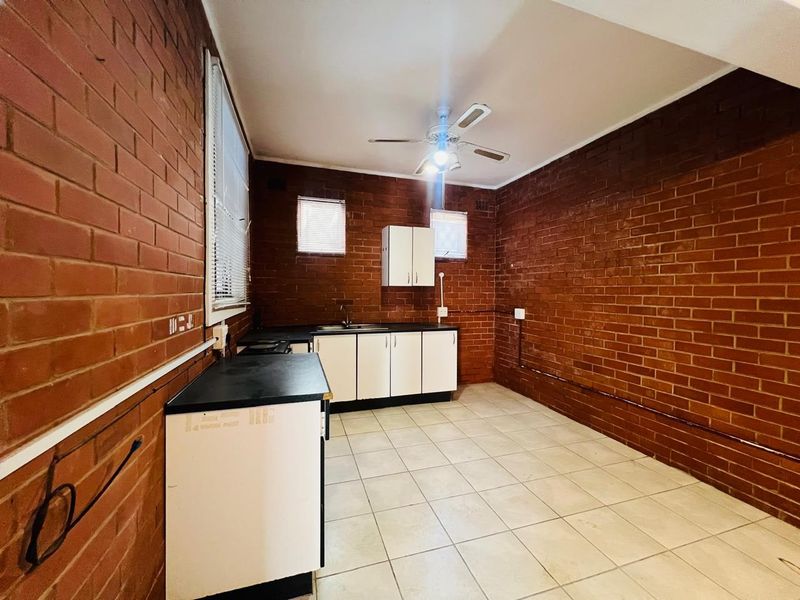 A functional kitchen featuring exposed brick walls, tiled flooring, and basic cabinetry with a stainless steel sink, offering potential for modern renovation.