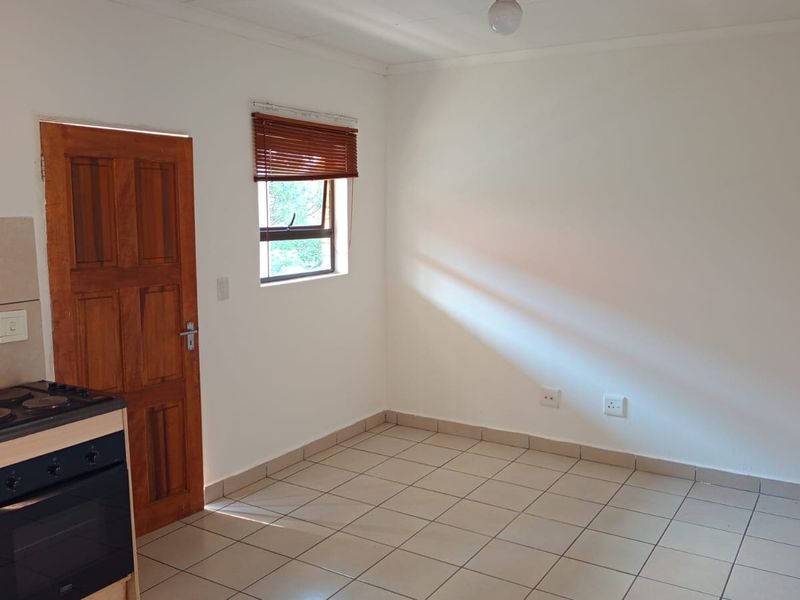 A compact, empty kitchen area featuring tiled flooring, a built-in oven with hob, and a wooden door leading to an adjacent space.