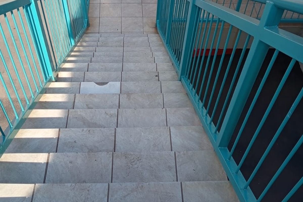 An exterior view of a tiled staircase with metal railings leading to an apartment entrance, featuring brick wall construction.