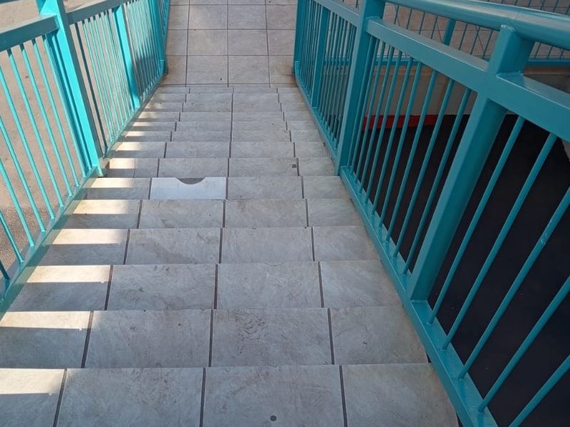 An exterior view of a tiled staircase with metal railings leading to an apartment entrance, featuring brick wall construction.