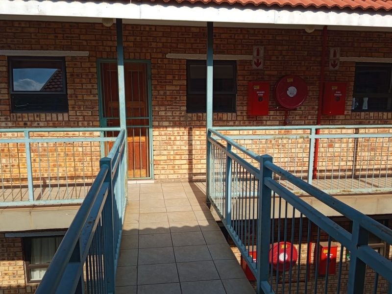 Exterior view of an apartment building walkway featuring brick facade, metal balustrades, and installed fire safety equipment.