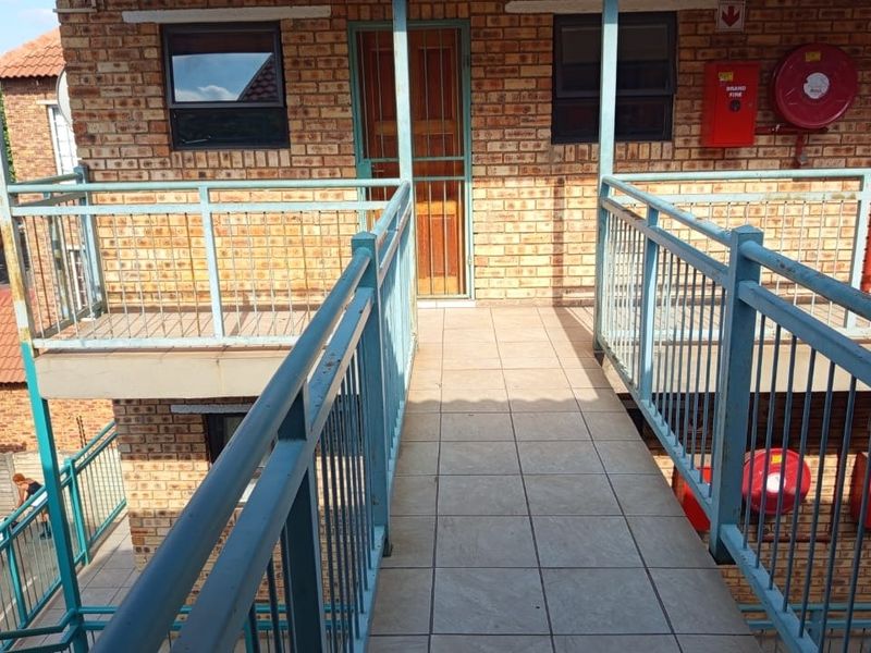 Exterior view of an apartment building walkway featuring brick facade, tiled flooring, and metal safety railings with integrated fire safety equipment.