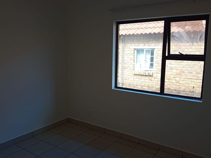 An empty bedroom featuring neutral tiled flooring and a large aluminium-framed window providing natural light.
