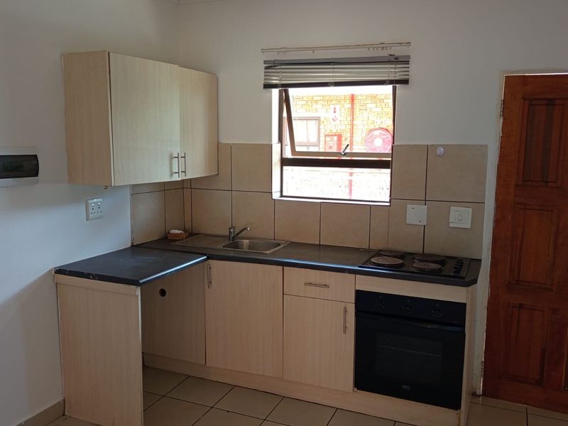A compact kitchen featuring light-toned laminate cabinetry, a built-in oven with electric hob, tiled splashbacks, and tiled flooring.