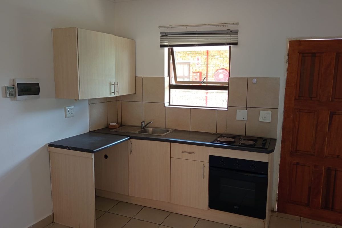 A compact kitchen featuring light-toned laminate cabinetry, a built-in oven with electric hob, tiled splashbacks, and tiled flooring.