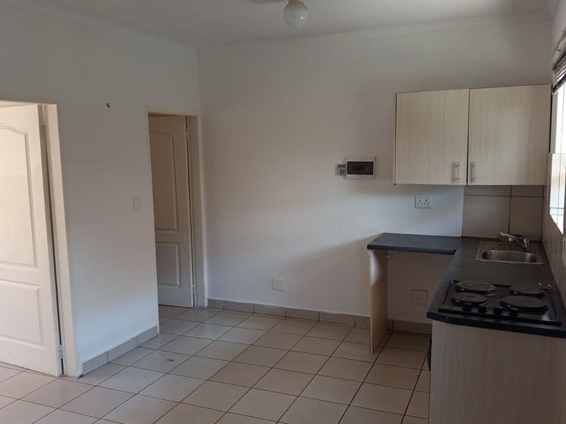 A functional, empty kitchen featuring tiled floors, built-in cabinetry, a stainless steel sink, and an electric hob.