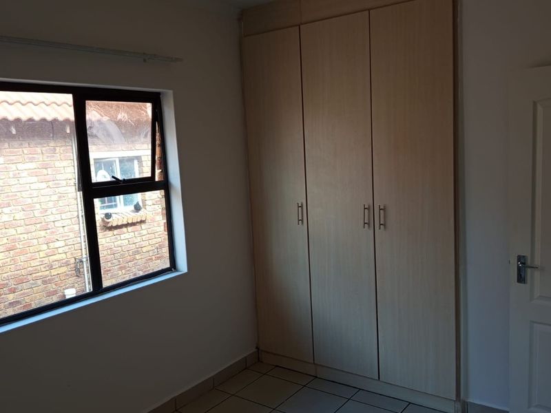 A clean, empty bedroom featuring built-in cupboards, tiled flooring, and an aluminium-framed window overlooking the exterior.