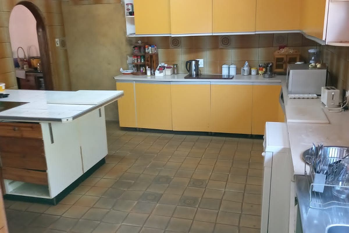Spacious kitchen featuring dated yellow cabinetry, a central island, tiled flooring, and a tiled backsplash, offering significant potential for a modern renovation.