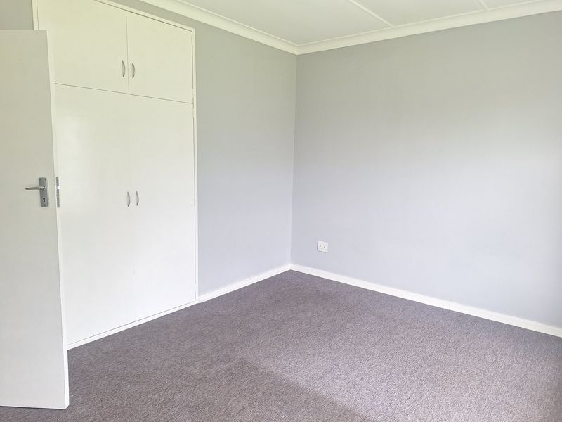 A clean, empty bedroom featuring neutral grey walls, grey carpeting, and built-in storage cupboards.