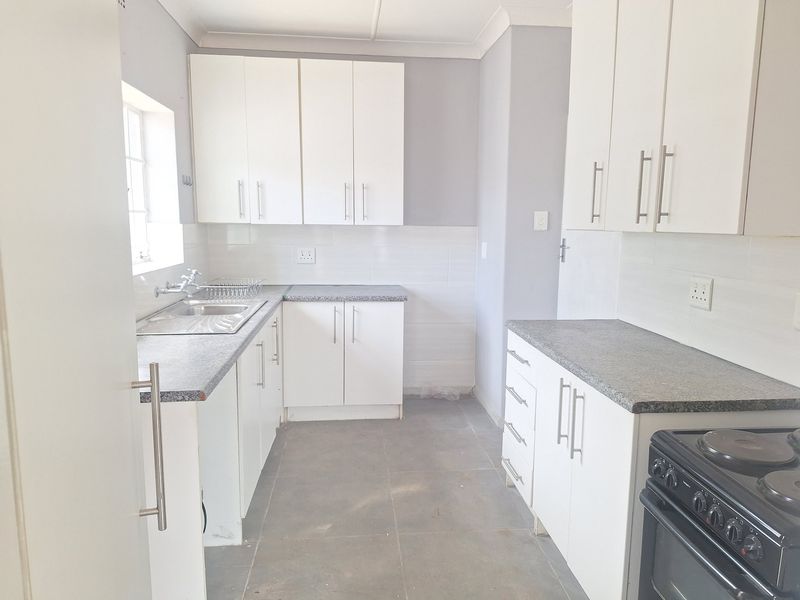 A clean, functional kitchen featuring white cabinetry, granite-look countertops, tiled backsplash, and tiled flooring, providing a neutral canvas for personalization.