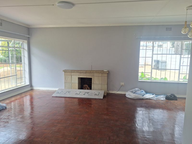 Spacious living room featuring polished parquet flooring, a central stone fireplace, and large windows with security bars, offering a bright and open layout.
