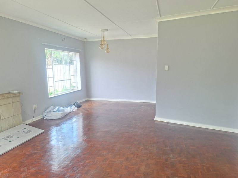 A bright, empty living room featuring polished parquet flooring, a fireplace, and large windows with security bars.