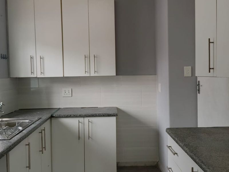 A clean, functional kitchen featuring white cabinetry, granite countertops, a stainless steel sink, and a tiled backsplash.