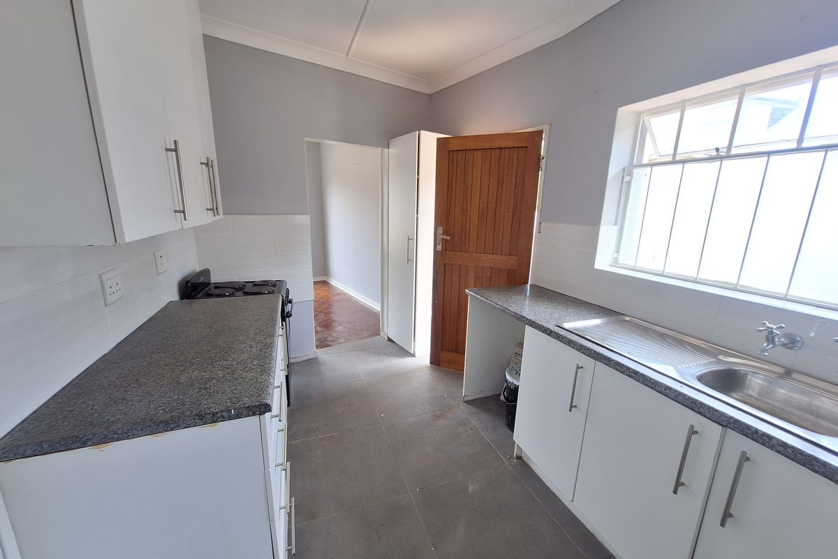 A functional kitchen featuring white cabinetry, granite-look laminate countertops, a stainless steel sink, and tiled flooring, offering a clean and practical workspace.