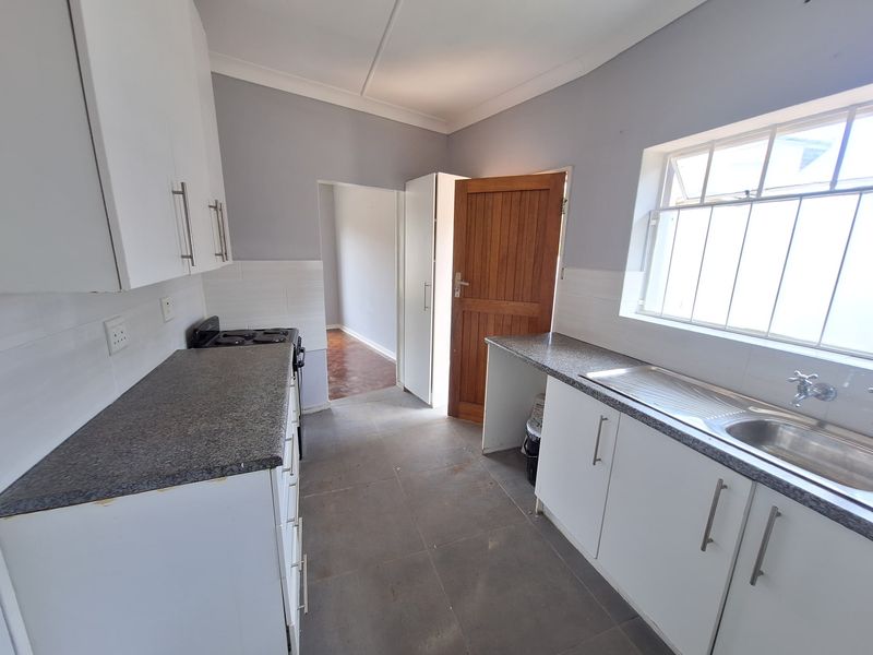 A functional kitchen featuring white cabinetry, granite-look laminate countertops, a stainless steel sink, and tiled flooring, offering a clean and practical workspace.