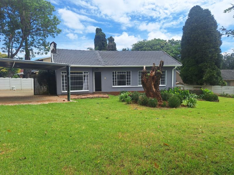 Front view of a single-story house featuring a tiled roof, attached carport, and a spacious front garden with a paved driveway.
