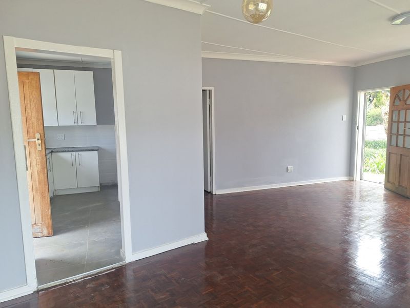 Open plan living area featuring polished parquet flooring and coved cornicing, with an adjacent kitchen area visible through the doorway.