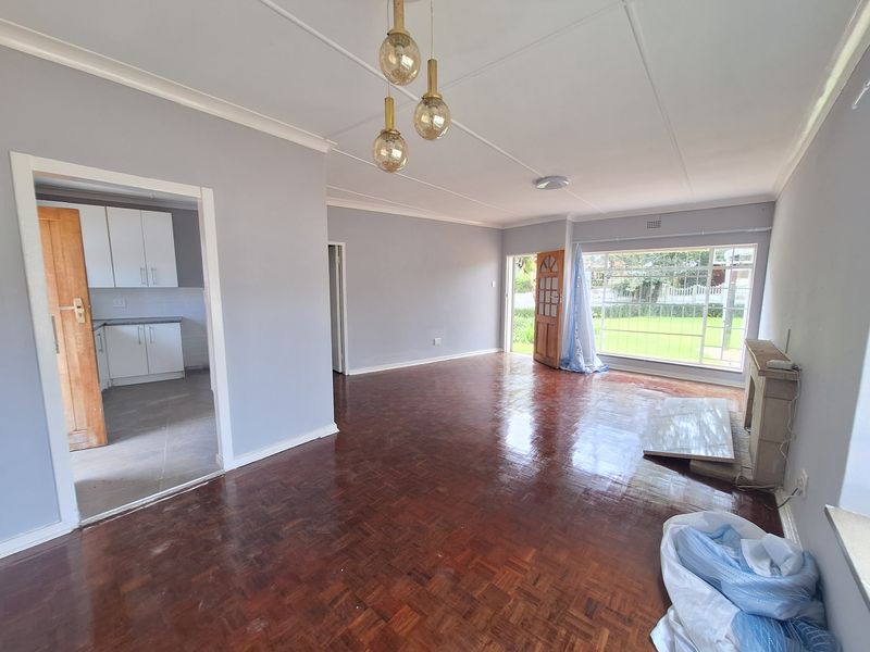 Spacious living room featuring polished parquet flooring, a fireplace, and large windows providing natural light, with an adjacent view into the kitchen area.