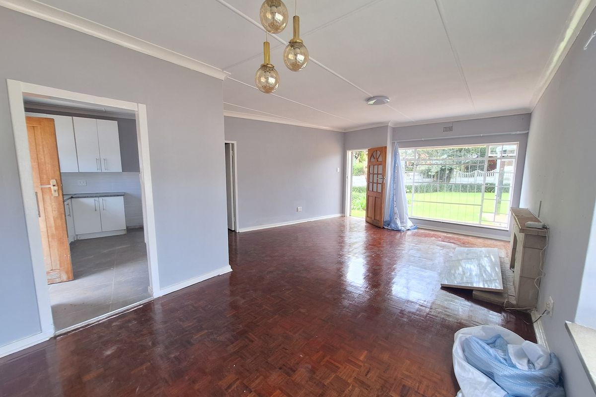 Spacious living room featuring polished parquet flooring, a fireplace, and large windows providing natural light, with an adjacent view into the kitchen area.
