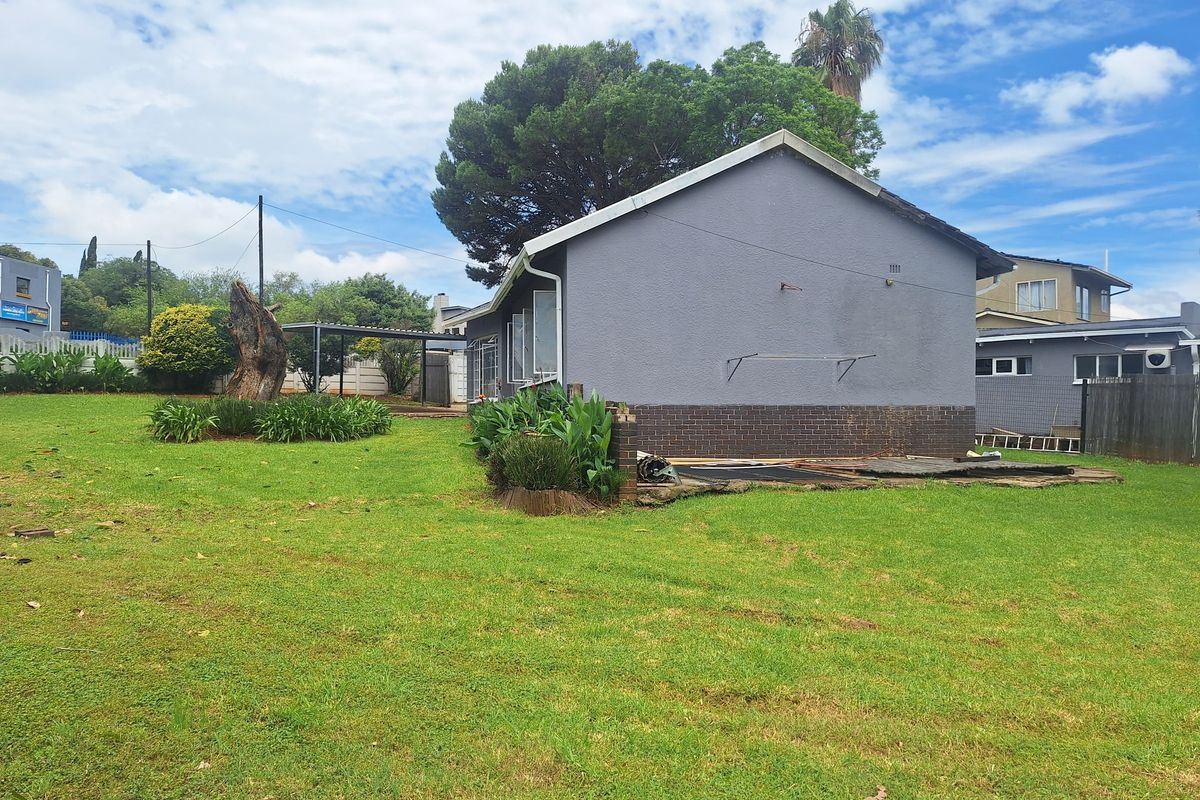 Rear view of the house showing a large lawn, plastered exterior walls with a brick base, and an area where patio paving has been removed.