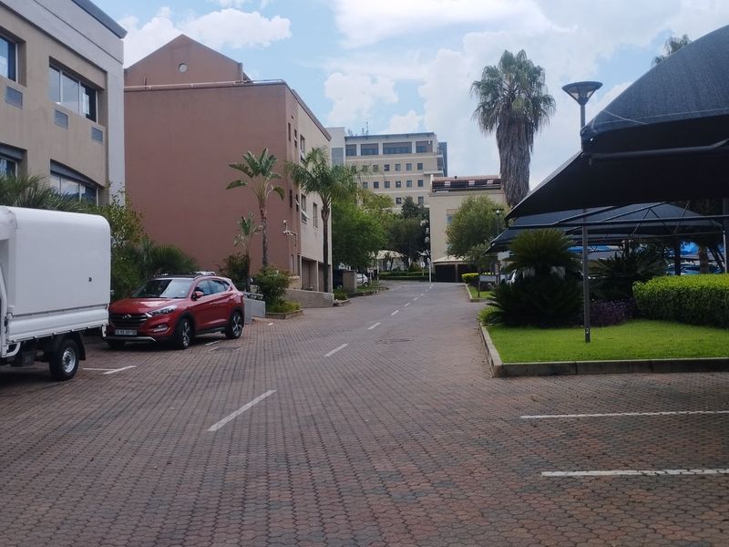 Exterior view of a commercial property complex featuring a paved driveway, landscaped garden areas, and covered parking bays.