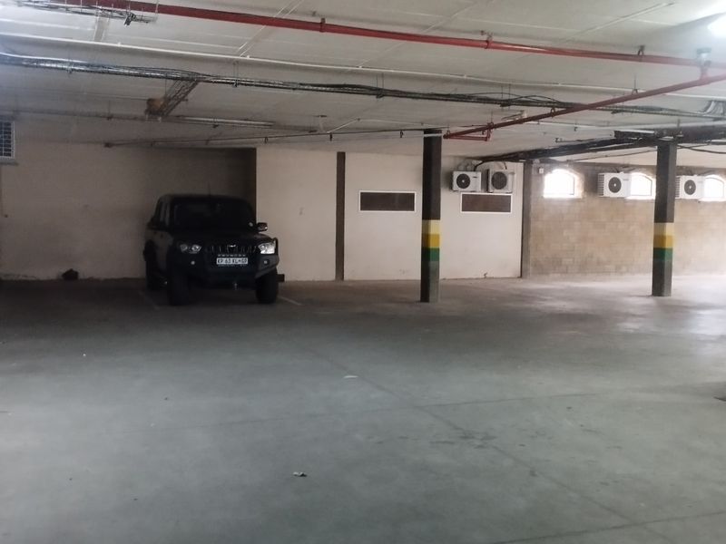 A spacious commercial basement parking area featuring concrete flooring, exposed fire sprinkler systems, and multiple wall-mounted air conditioning units.