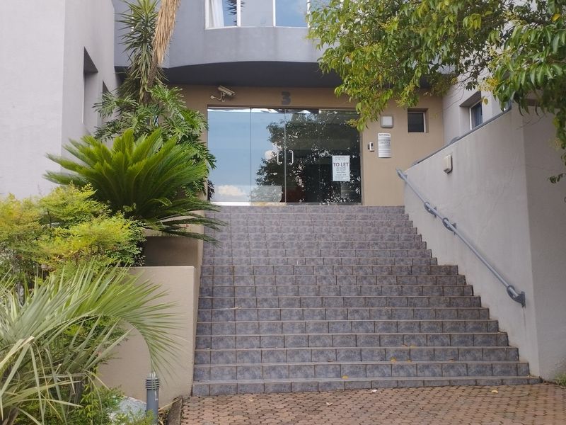 Front entrance of a commercial building featuring a tiled staircase leading to glass double doors with security and intercom systems.