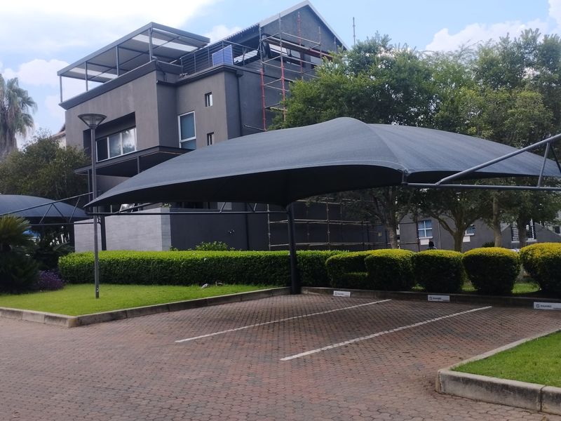 Exterior view of a commercial property featuring a paved parking area with shade cloth carports and landscaped garden beds.