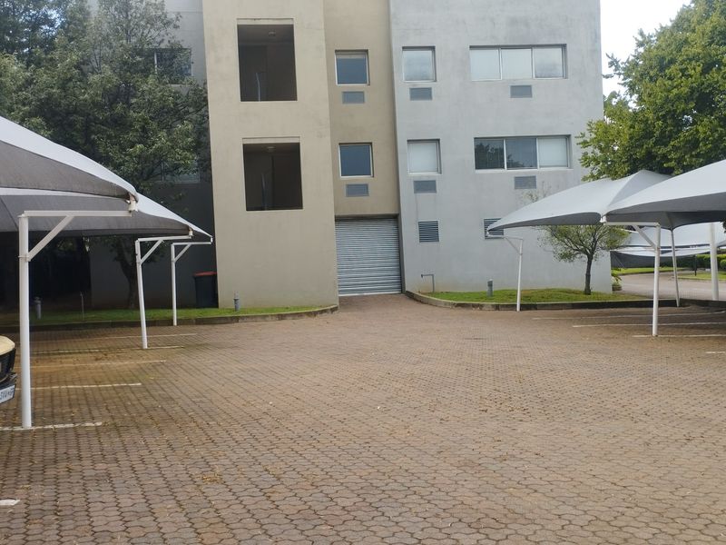 Commercial property exterior featuring a paved parking area with shade cloth carports and a secure roller shutter door access point.