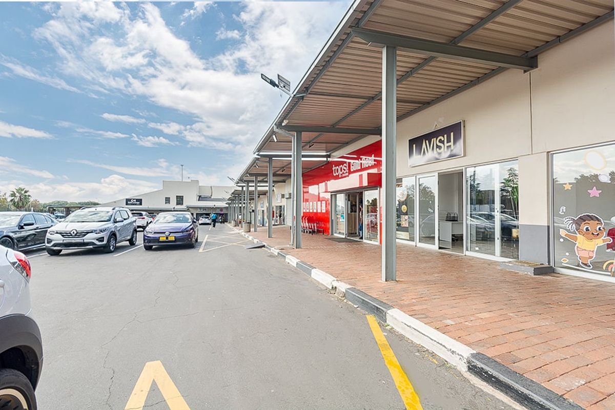 Exterior view of a commercial retail strip center featuring covered walkways, glass storefronts, and paved parking area.