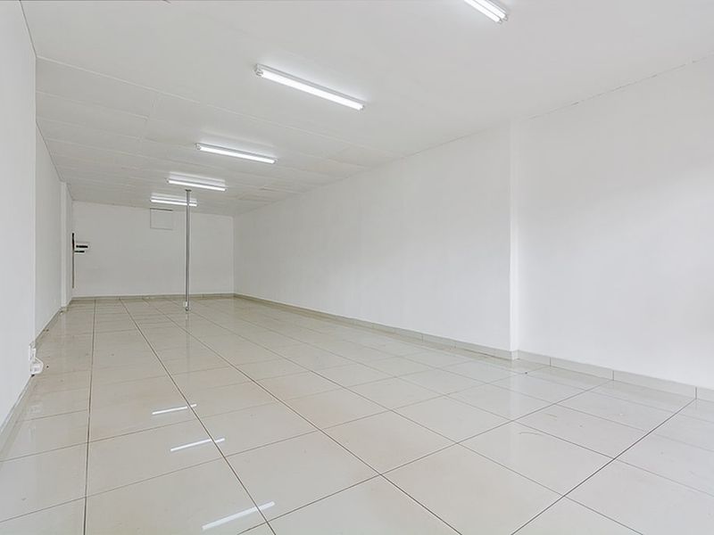A clean, vacant commercial office space featuring bright fluorescent lighting, neutral tiled flooring, and an open-plan layout suitable for various business configurations.