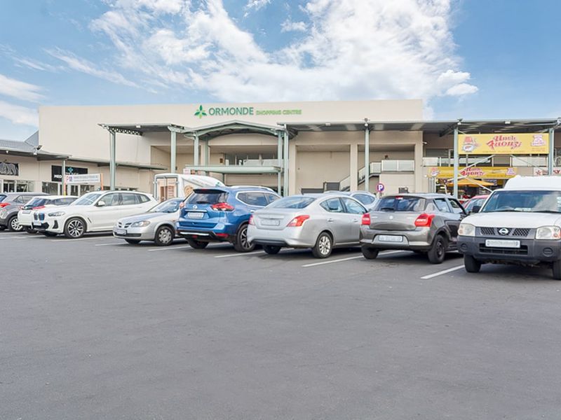 Front view of the Ormonde Shopping Centre featuring a large asphalt parking area and a prominent commercial building facade with metal canopy structures.