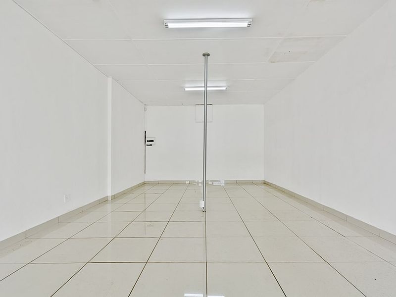 A vacant commercial office space featuring tiled flooring, a central support pole, and functional overhead fluorescent lighting.