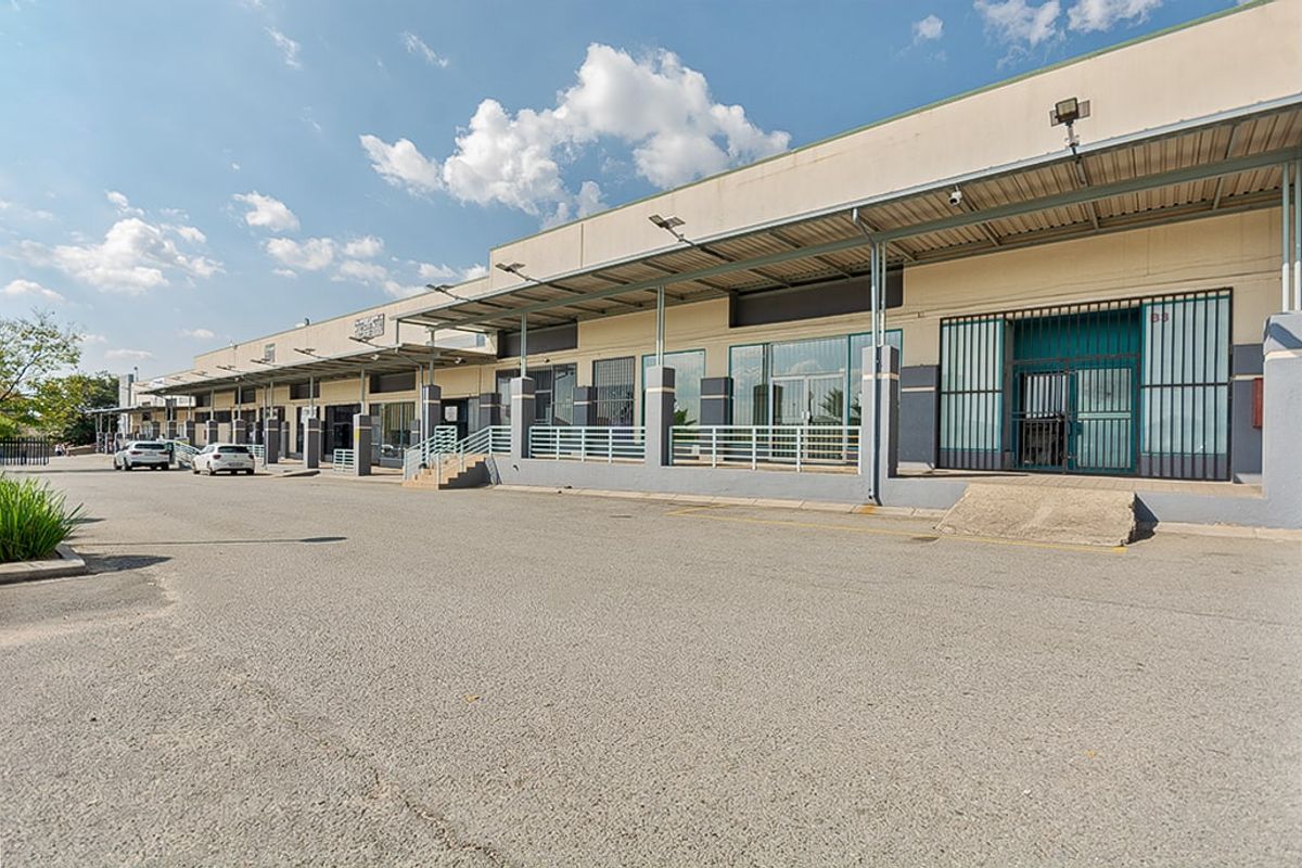 Commercial property exterior featuring a row of storefronts with metal canopy coverage, security gates, and an expansive asphalt parking area.