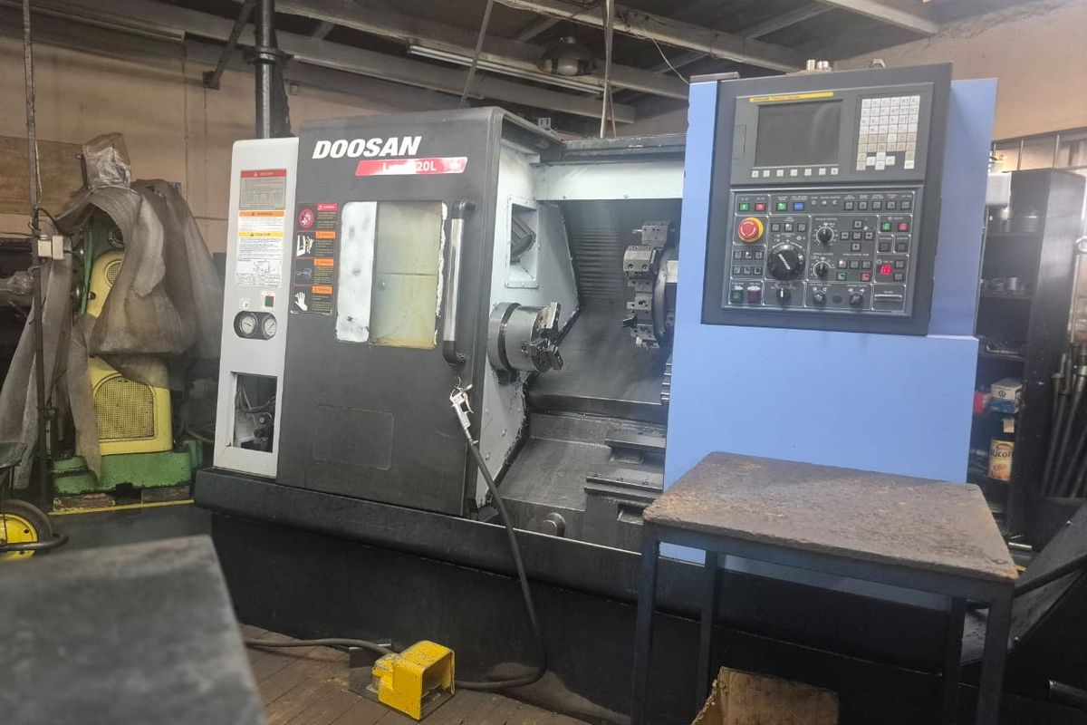 Industrial workspace featuring a Doosan CNC lathe machine with integrated control panel, situated in a functional workshop environment.