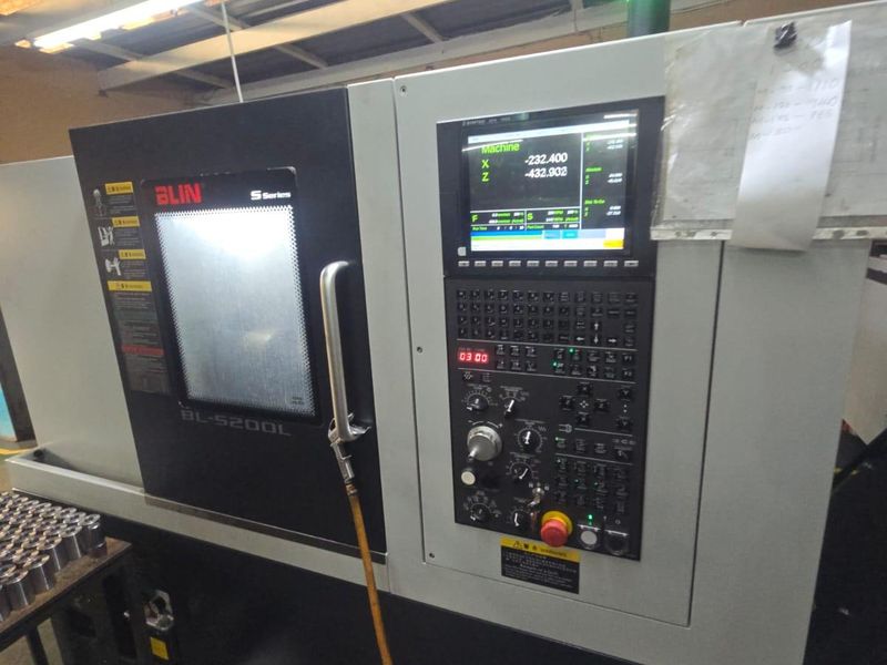 Industrial workspace featuring a BLIN S-Series CNC lathe machine with integrated control panel and overhead industrial lighting.