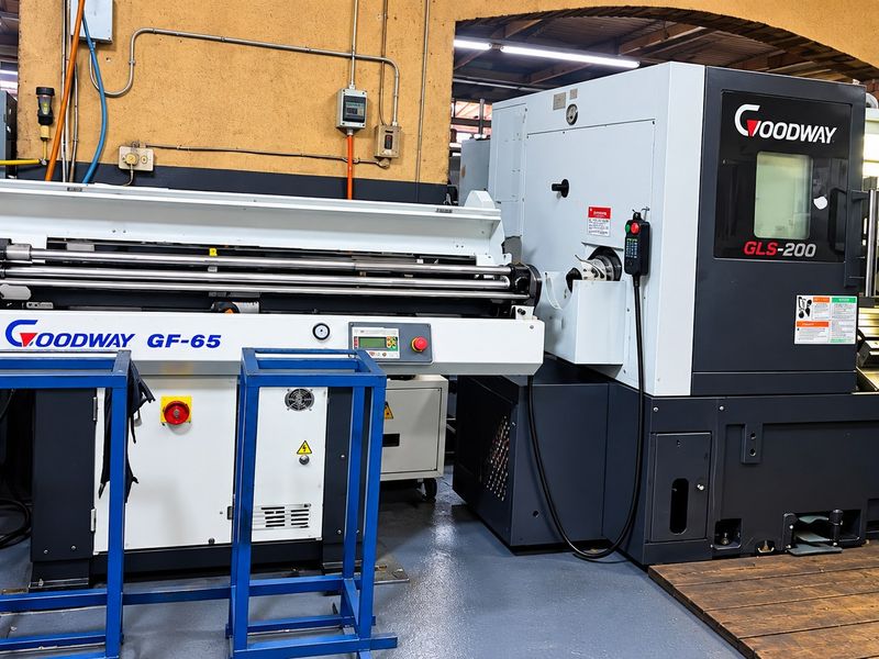Industrial workshop space featuring a Goodway CNC lathe and bar feeder system, set on durable epoxy flooring with exposed electrical infrastructure.