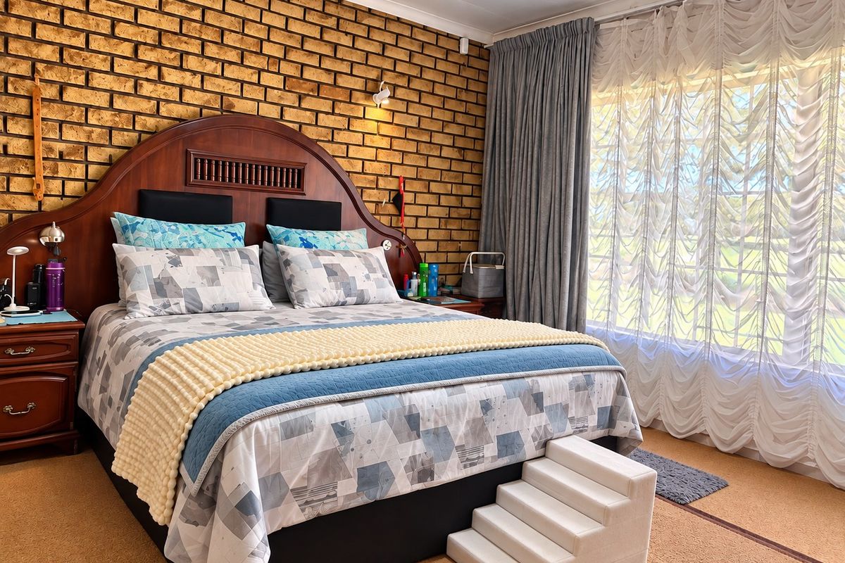 A spacious bedroom featuring a prominent exposed brick feature wall, large window with layered curtains, and neutral carpeting.