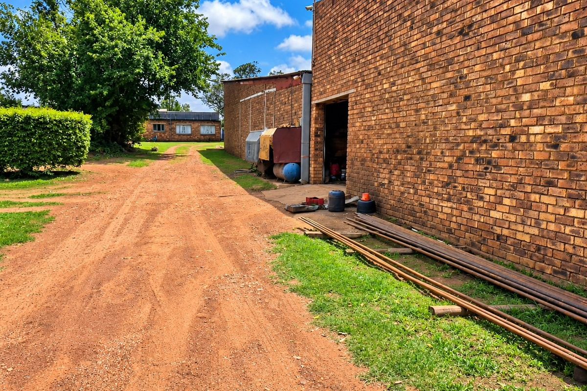Rear exterior view of a commercial brick building featuring an unpaved access road and surrounding landscaped grounds.