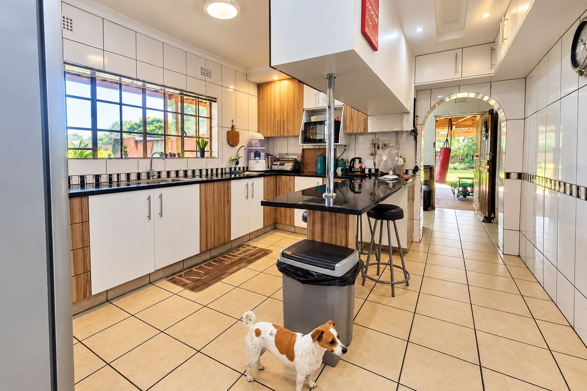 A functional kitchen featuring built-in cabinetry, granite countertops, a breakfast bar, and tiled finishes, with an archway leading to an outdoor area.