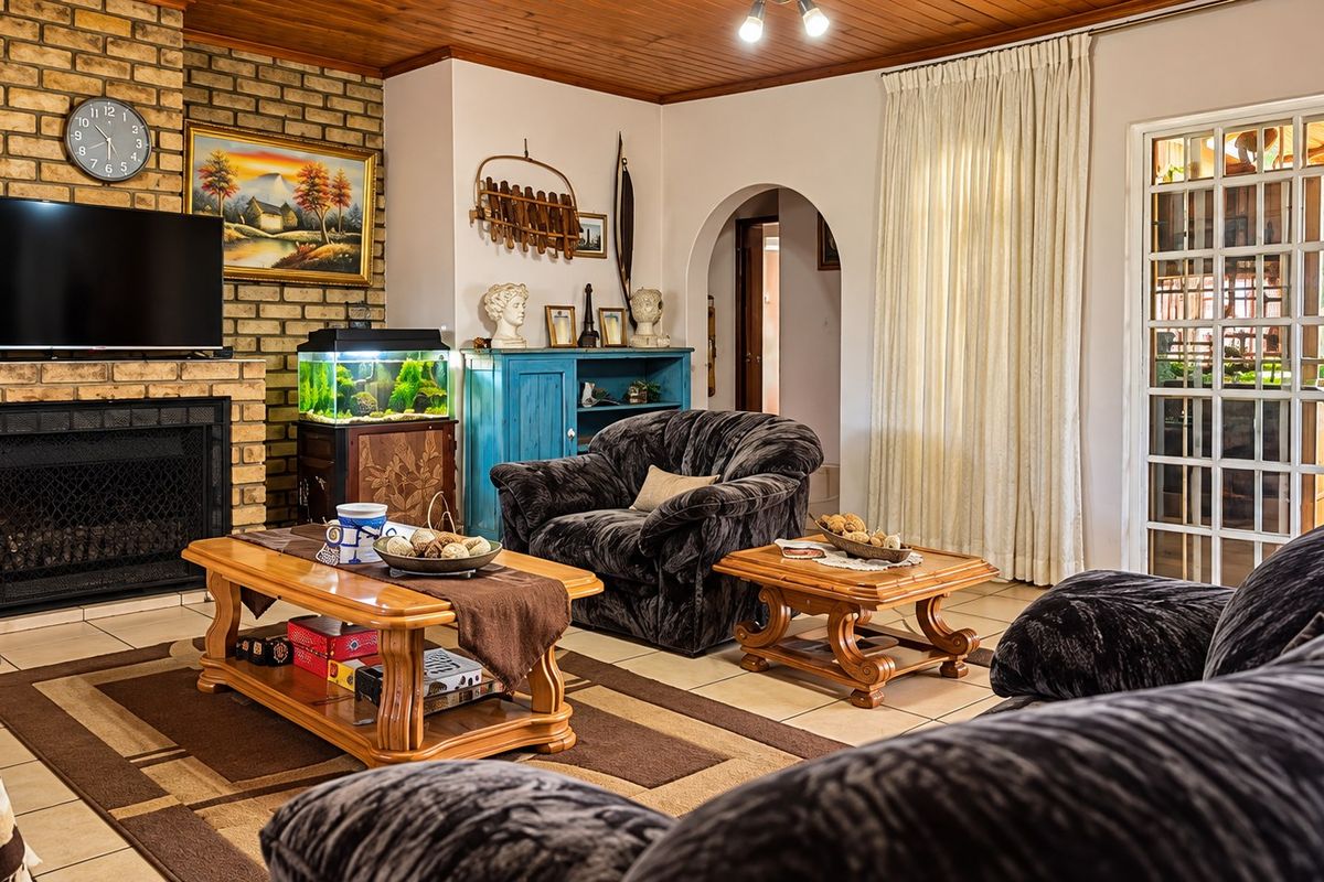 A cozy living room featuring a prominent brick fireplace, timber-clad ceiling, and tiled flooring, with an arched entryway leading to other areas of the property.