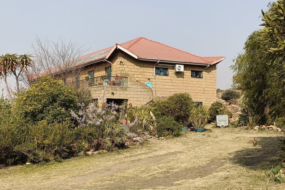A view of the rear elevation of a sandstone farmhouse featuring a tiled roof, balcony, and established garden surroundings.