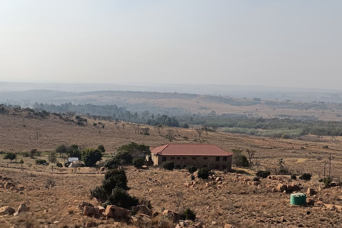 An elevated aerial view of the farm property, showcasing the main dwelling, surrounding rocky landscape, and open rural terrain.