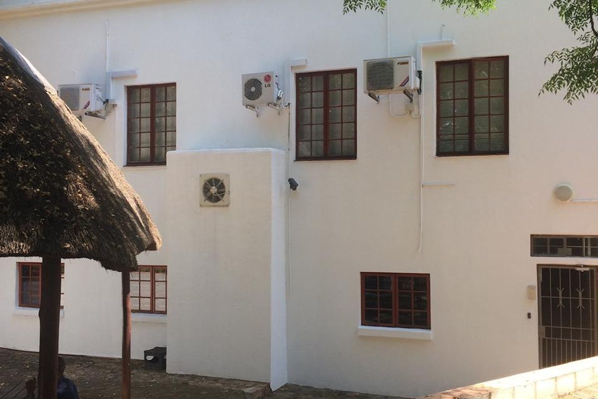 Rear exterior view of a commercial building featuring white plastered walls, multiple window units, and wall-mounted air conditioning units.