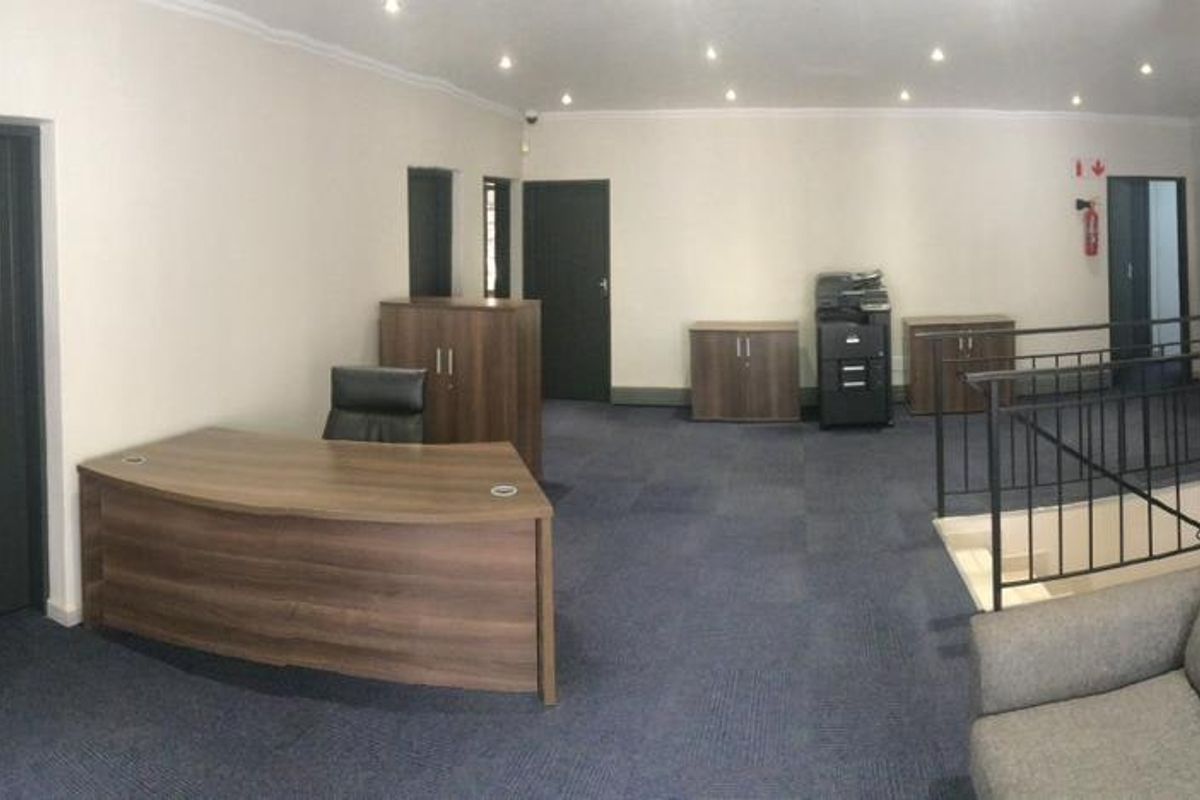 A spacious commercial office area featuring carpeted flooring, recessed ceiling lighting, and a staircase with a metal railing.