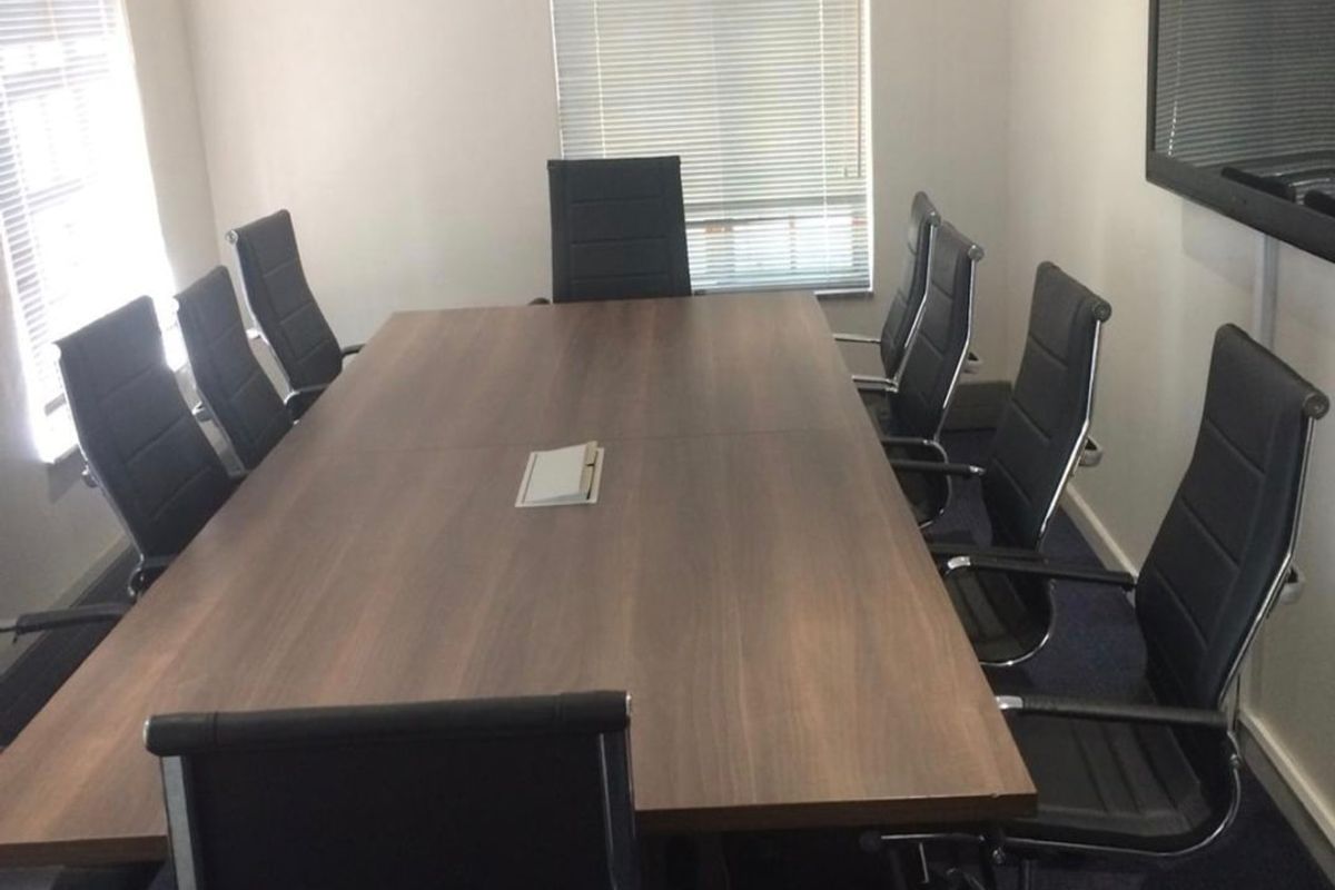 A professional boardroom featuring a large central meeting table, wall-mounted air conditioning unit, and venetian blinds on the windows.
