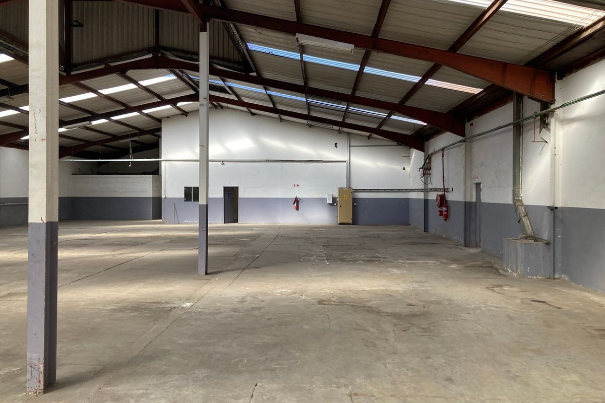 Spacious industrial warehouse unit featuring high ceilings with exposed steel trusses, skylights for natural light, and durable concrete flooring.