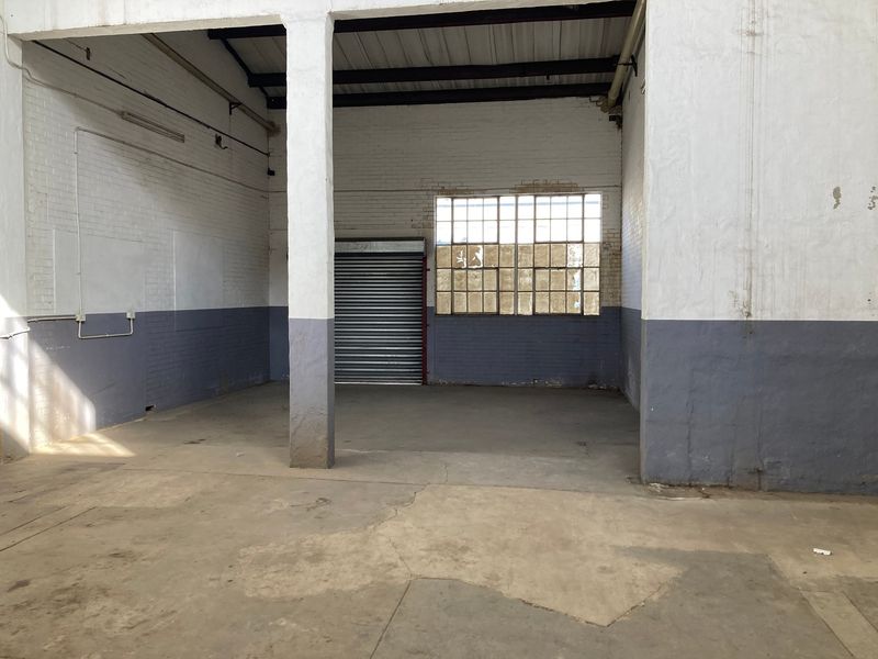 Spacious industrial utility area featuring concrete flooring, exposed brick walls, a steel support column, and a secure roller shutter door.