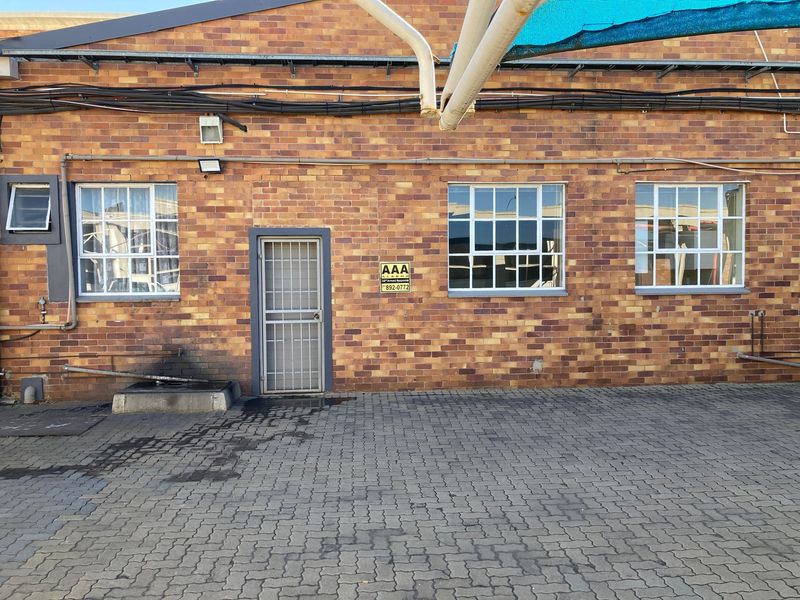 Exterior view of an industrial brick building featuring a security gate, steel-framed windows, and paved ground area.